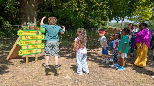 A group of children and parents follow the play challenge on a Pokémon Mega Evolution board